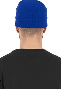 Căciulă tricotată albastră, cu o textură canelată și cu o manșetă pliată, purtată de o persoană. Un tricou negru este vizibil sub căciulă.