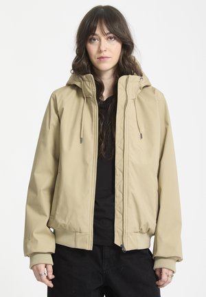 Veste à capuche beige avec fermeture éclair, poignets côtelés et texture lisse. Comprend des cordons de serrage sur la capuche et des poches latérales.
