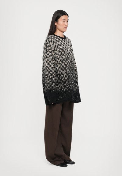 Oversized black and cream patterned sweater with a gradient texture, paired with dark brown wide-leg trousers and black shoes.