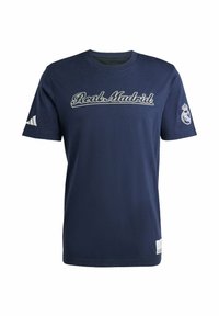 Camiseta de algodón azul marino con "Real Madrid" bordado en blanco, con el logotipo de Adidas en blanco en la manga izquierda y el emblema del equipo en la derecha.