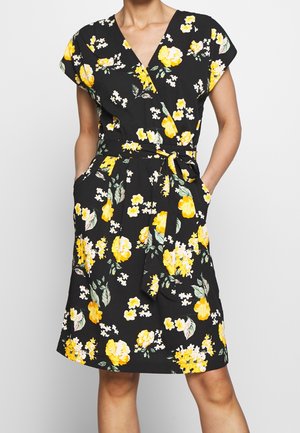 Vestido negro con estampado floral que presenta flores amarillas, mangas cortas tipo cap sleeve, diseño envolvente, cinturón a la cintura y bolsillos. La tela tiene una textura suave.