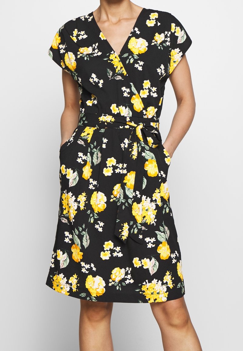 Černé květinové šaty s žlutými květy, krátkými rukávy typu cap, zavinovacím designem, páskem v pase a kapsami. Látka má hladkou texturu.