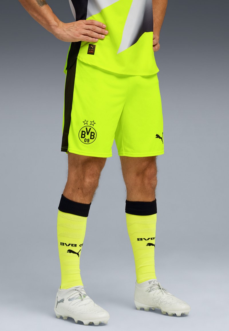 Pantaloni da calcio giallo neon con dettagli neri e logo BVB. Abbinati a calze gialle e scarpe bianche con design testurizzato.