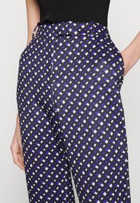 Pantalones estampados que presentan una base de color azul marino oscuro con un patrón geométrico en púrpura, blanco y negro. Tela suave con un corte ajustado.
