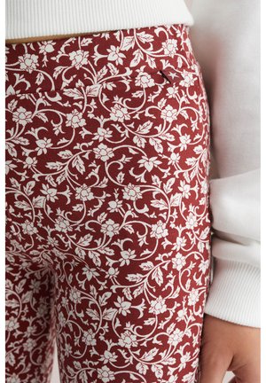 Tissu à motifs floraux rouges avec des fleurs et des feuilles blanches, présentant un gros plan d'une ceinture et des détails de couture. Matériau doux et texturé.