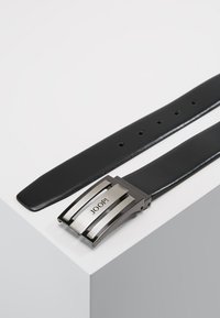Cinturón de cuero negro con una hebilla rectangular de plata pulida marcada como "JOOP!" y múltiples agujeros de ajuste en la correa para un mejor ajuste.