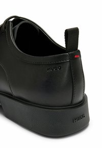 Scarpa in pelle nera con suola in gomma nera testurizzata, dotata di una linguetta posteriore e logo stampato. Parte superiore liscia con dettagli di cucitura discreti.
