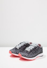 Scarpe sportive con una tomaia a motivo nero e grigio, lacci grigi e una suola rosa, con intersuola bianca e dettagli testurizzati.
