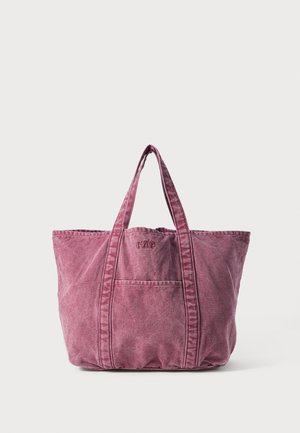 Rosa kanvas tote bag med doble håndtak, med en frontlomme og embossert logo. Myk tekstur med synlige sømmer.