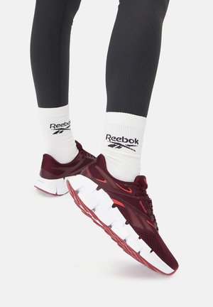 Buty sportowe Reebok z ciemnoczerwonym siateczkowym wierzchem, białą piankową podeszwą i czerwonymi akcentami. W komplecie białe skarpetki z logo Reebok.