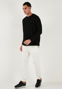Camisa negra de manga larga con cuello redondo, combinada con pantalones jogger blancos y zapatillas negras, con un logo en la camisa.