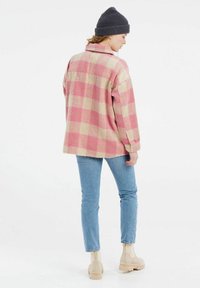 Camisa de franela en un patrón de cuadros rosa y beige, de corte holgado, con una textura suave. Combinada con jeans de botones claros y botas de tobillo beige.