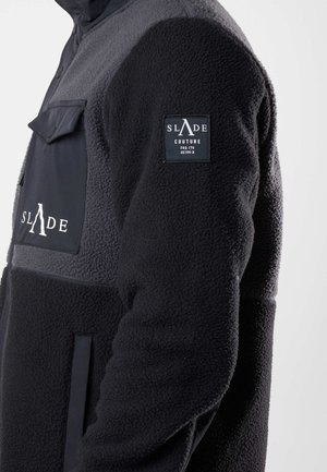 Black and gray fleece jacket featuring a zip closure, a chest pocket, and a logo patch on the sleeve. Soft texture with contrasting colors.