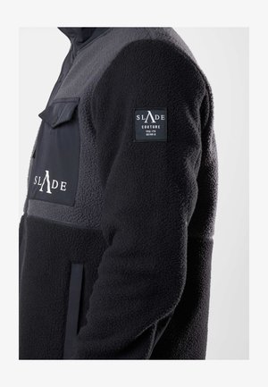 Black and gray fleece jacket featuring a zip closure, a chest pocket, and a logo patch on the sleeve. Soft texture with contrasting colors.