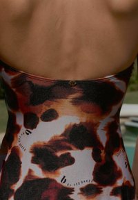 Maillots de bain avec un design animalier brillant dans des tons de marron et d'orange. Présente une découpe minimale au dos et un petit logo doré.
