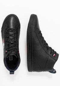 Zwarte hoge sneakers van soepel leer met textuurpanelen aan de zijkant, voorzien van contrasterende witte veters en een kleine rode, witte en blauwe accent.