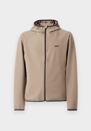 Beige hettejakke med glidelås foran, sorte detaljer og logo på brystet. Laget av et glatt, stretchy stoff med en tettsittende design.