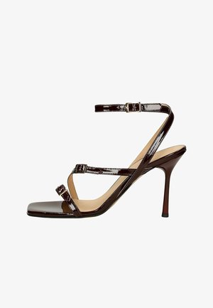 Brown patent leather high-heeled sandal with a square toe, cross straps, ankle strap with a buckle, and a slender heel.