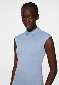 Hihaton poolopaita vaaleansinisellä sävyllä, jossa on teksturoitu, aaltomainen kuvio. Ominaisuuksina kauluspaita ja pieni logo kauluksessa.