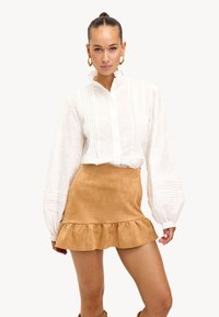 Witte textuur blouse met een hoge kraag en knoopsluiting, gecombineerd met een tan suede mini rok met een ruchesrand.