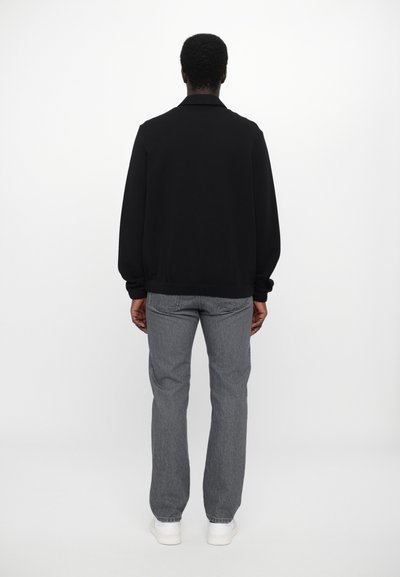 Sweatshirt noir à coupe décontractée, avec des poignets et un ourlet côtelés, associé à un jean gris et des baskets blanches, vu de dos.
