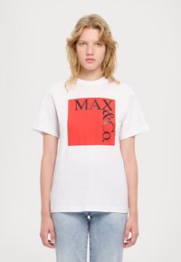 Hvit bomull T-skjorte med et stort rødt kvadrat med teksten "MAX & Co." i svart, korte ermer og løs passform. Denim jeans synlige.