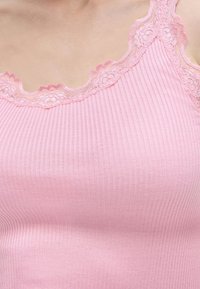 Κοντινή λήψη ριμπ ροζ κορσέ με δαντελένιο περίγραμμα γύρω από το ντεκολτέ και τους ιμάντες σε γυμνό δέρμα.