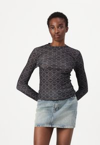 Long-sleeve, fitted black shirt with a geometric pattern in grey. Features a crew neck and smooth texture, paired with a light denim skirt.