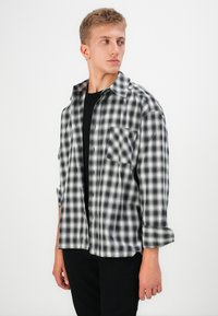 Black and white plaid flannel shirt with a collar, two chest pockets, and button front. The model wears a black T-shirt underneath.