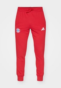Røde joggebukser laget av bomullsmiks, med snøring i livet, ribbestrikkede mansjetter og en rund logo på venstre lår med hvite detaljer.