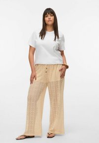 Hvit kortermet t-skjorte kombinert med lys beige, vide bukser med blondermønster og snor i livet. Enkle flip-flops.