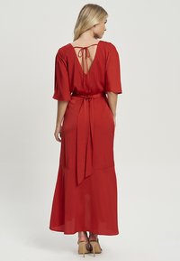 Červené maxi šaty z lehkého materiálu mají výstřih do V se zavazováním, krátké rukávy a splývavou sukni. Hladká textura a elegantní střih.