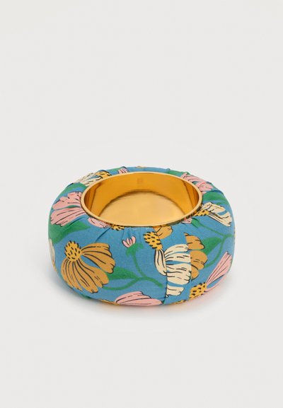 Στρογγυλό χρυσό μεταλλικό μπολ με μαλακό μπλε υφασμάτινο κάλυμμα που φέρει μεγάλα ροζ, κίτρινα και λευκά λουλουδένια σχέδια.