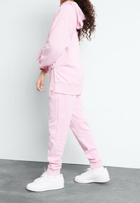 Rosa huvtröja och matchande sweatpants. Mjuk tyg, avslappnad passform. Vita sneakers fulländar outfiten. Enkel, sammanhängande design.