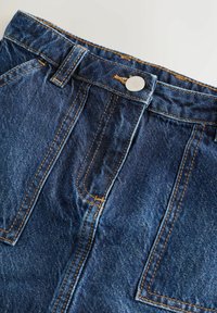 Denim tkanina u tamnoplavoj boji s kontrastnim žutim šavovima, s metalnim gumbom, gornjim zatvaranjem i dva prednja džepa.