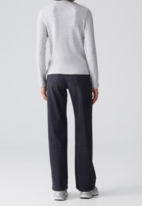 Szary, teksturowany sweter z długimi rękawami, zestawiony z ciemnymi jeansami o klasycznym kroju i prostych nogawkach. Obuwie stanowią szare sneakersy.