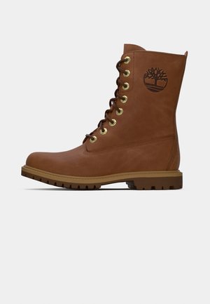 Braune Leder Schnürstiefel mit Gummisohle und geprägt Baum-Logo am Knöchel, Seitenansicht auf weißem Hintergrund.