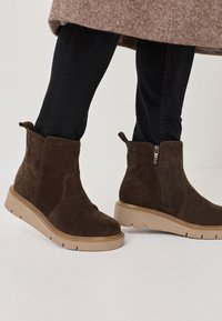 Bottines en suédine marron avec fermeture éclair latérale et tirant, présentant une semelle épaisse beige et un motif texturé subtil.