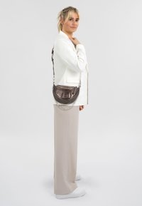 Borsa a tracolla in pelle bronzo metallico con forma curva, hardware in catena e tracolla, caratterizzata da una finitura testurizzata e chiusura con zip.