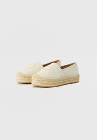 Bež espadrile s platnenim gornjim dijelom, tkanim jutenim potplatom i izvezenim cvjetnim detaljem sprijeda. Model koji se nosi bez vezivanja s zaobljenim vrhom.