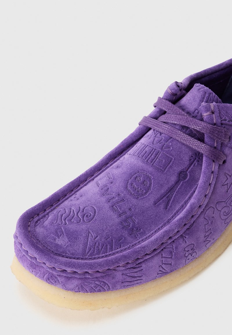 Chaussure en daim violet avec des motifs embossés, des accents cousus et une texture douce. Possède une semelle en caoutchouc et un laçage à l'avant.