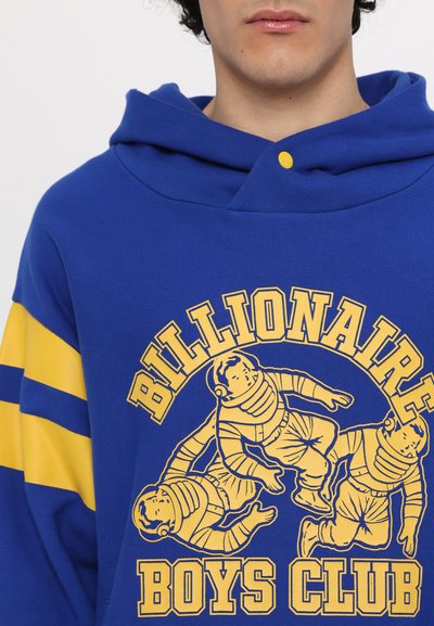 Blaues Hoodie mit gelben gestreiften Ärmeln. Präsentiert einen grafischen Druck von drei Astronauten und dem Text "Billionaire Boys Club" in fettem Gelb.