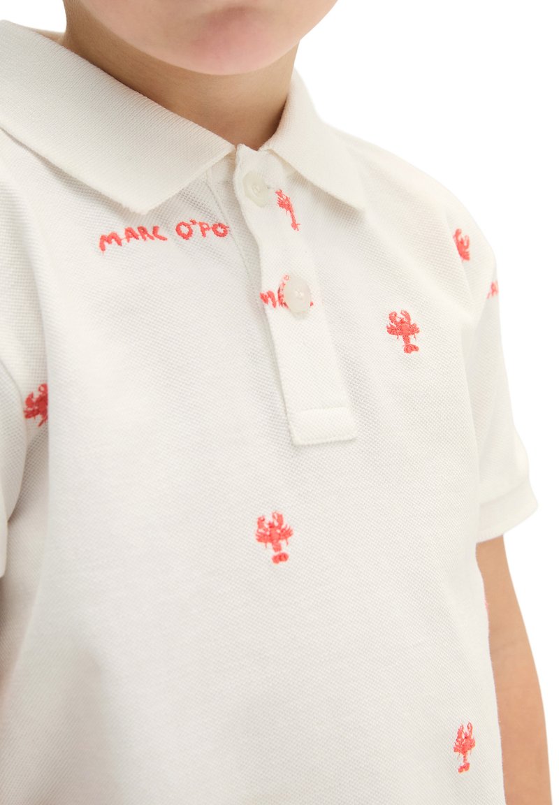 Enfant portant un polo blanc avec une petite broderie rouge en forme de homard et le texte « Marc O'Polo » près du col.