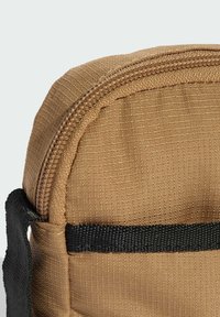 Borsa in tessuto beige con superficie testurizzata, dettaglio cerniera e tracolla nera. Forma arrotondata, costruzione robusta e elementi di colore a contrasto.