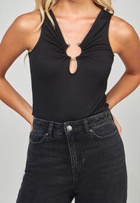 Svart ribbad bodysuit med en nyckelhålsöppning vid halsringningen, med samlade detaljer och silverfärgade metallaccenter. Matchad med högmidjade svarta jeans.