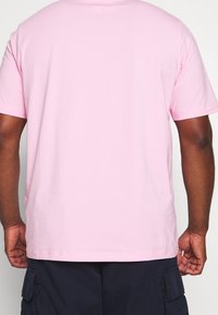 Camiseta de algodón rosa con mangas cortas y un bajo recto, con una textura suave y un diseño clásico de cuello redondo.