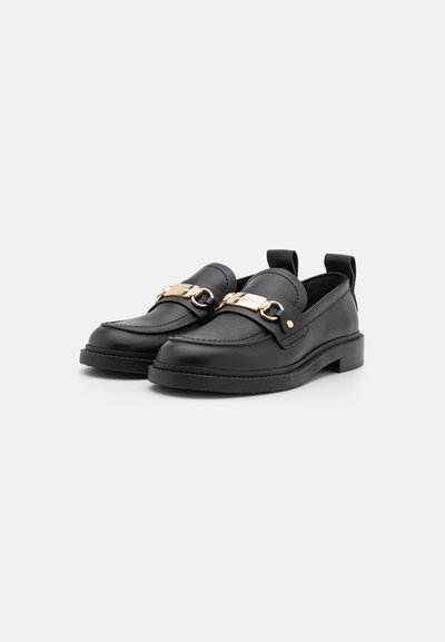 Mustad nahast loafers, mille esiosas on kuldsete ahelate detail, ümar varvas ning väike plokk konts; tekstuuriga pind ja minimaalne õmblus.