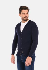 Cardigan blu navy in tessuto a maglia, con scollo a V, chiusura completa con bottoni, polsini e orlo a coste, abbinato a una t-shirt bianca e jeans.