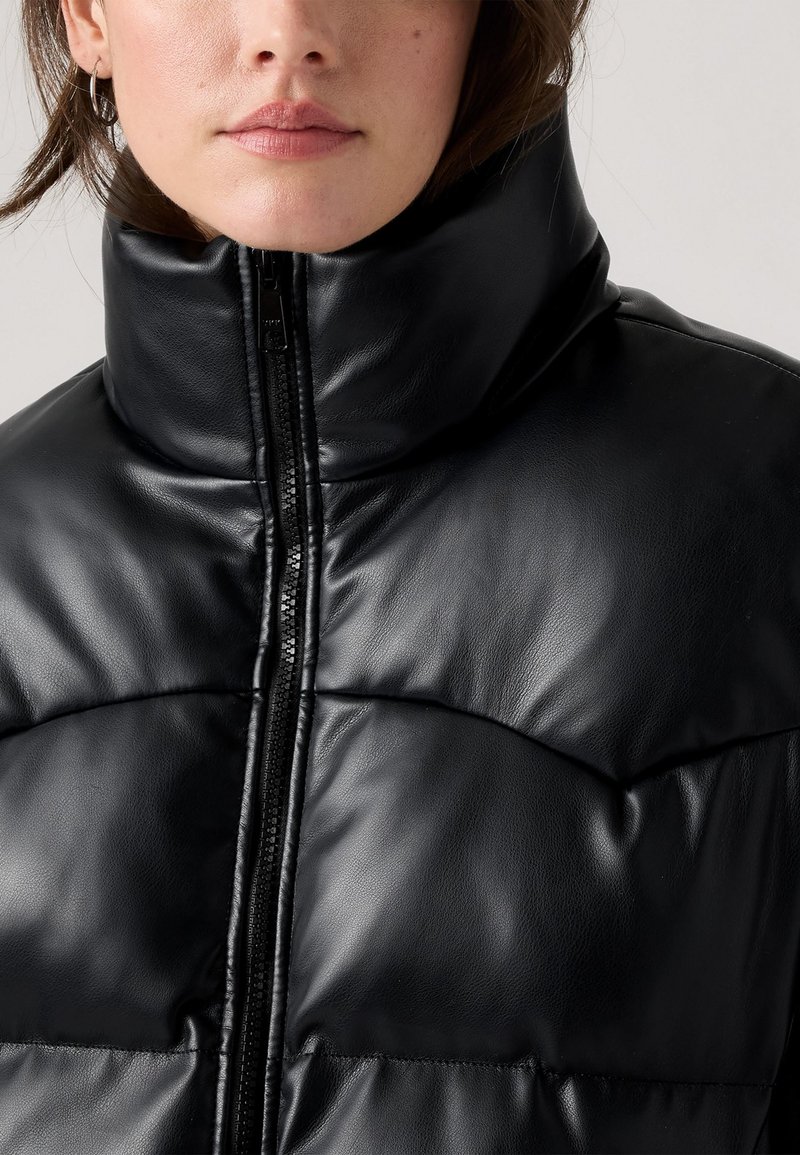 Giubbotto piumino nero con colletto alto, chiusura con zip e materiale liscio simile alla pelle, con dettagli trapuntati sul corpo.
