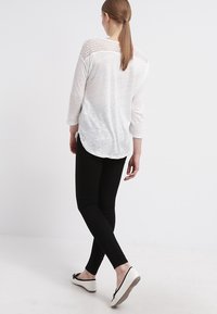 Bílý dlouhý rukáv top s texturovaným krajkovým zadním dílem, v kombinaci s černými legínami a černobílými plochými botami. Hladká tkanina s volným střihem.